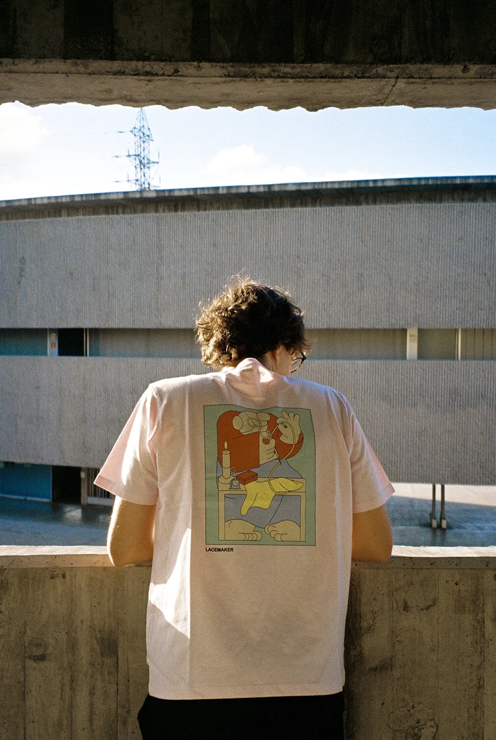 A person wearing a light pink Uniqlo T-shirt featuring a reimagined illustration of Vermeer’s “The Lacemaker” on the back. The design simplifies the original painting into bold, minimal shapes and a contrasting color palette, blending classical art with a modern graphic aesthetic. Photograph by Elena Navarro.