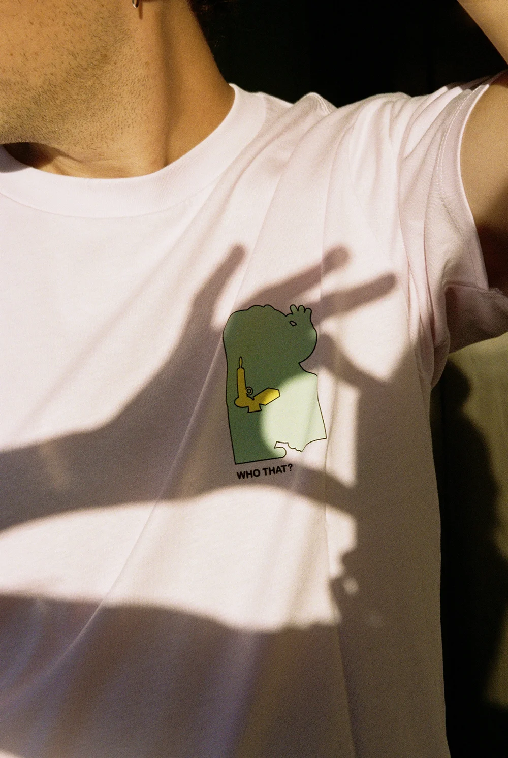 A close-up of the front of the Uniqlo T-shirt from the Jhon Boy x Louvre collaboration. The minimalist chest print features an abstract silhouette with a candle and text reading “WHO THAT?”, playing with negative space and simplified forms inspired by “The Lacemaker. Photograph by Elena Navarro.